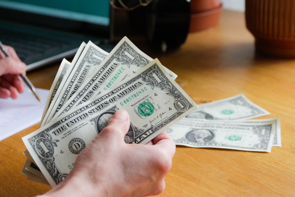 A hand holding several one dollar bills.