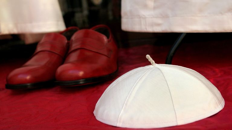 A Papal white skull cap and burgundy shoes are displayed in the Gammarelli's tailor shop window in Rome, April 14, 2005. Cardinals start choosing a new Pope next week, but the successor to John Paul will be all sewn up well before the secret conclave opens. Because the tailor Filippo Gammarelli has no clue as to who the new pope will be, the firm has made three versions of the same silk and wool outfit, in small, medium and large, to clothe the most lean or corpulent cardinal. Picture taken Apri
