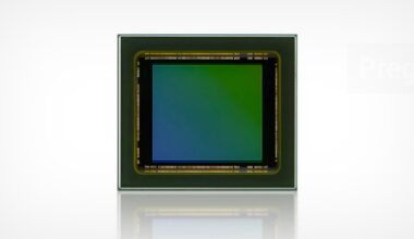 Close-up of a square electronic sensor chip with a green and blue gradient in the center, bordered by a metallic frame, set against a plain white background.