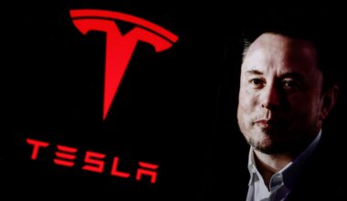 Elon Musk next to large red Tesla logo
