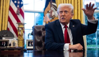 US-Präsident Donald Trump im Anzug mit roter Krawatte im Weißen Haus am Schreibtisch. Hinter ihm eine US-Flagge. Er gestikuliert gut gelaunt mit einer Hand.