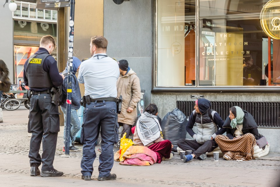 Two police officers checking the documents of immigrants sitting on the street.