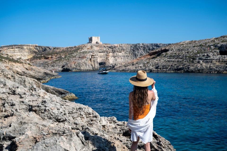 Woman in a straw hat overlooking a blue lagoon from a rocky cliff.