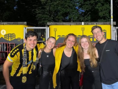 Group photo of five young adults in front of a yellow wall with stadium illustrations.