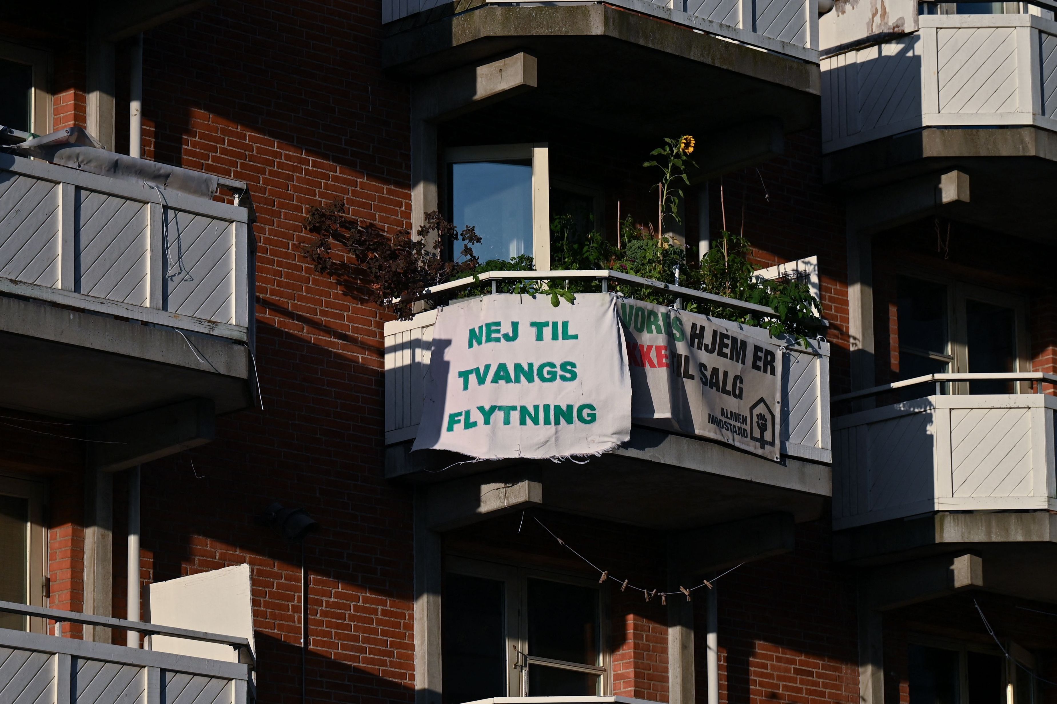 Banners reading "No to forced relocation" and "Our homes are not for sale" hang from balconies of a residential building.