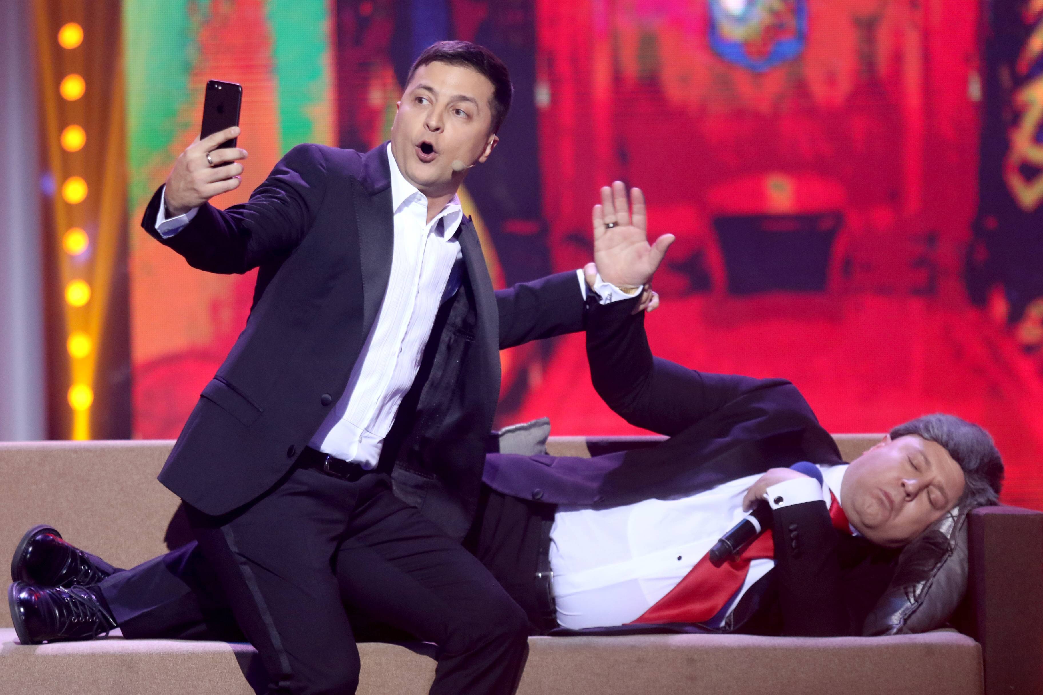 Volodymyr Zelenskyi taking a selfie while Oleksandr Pikalov sleeps on a couch.
