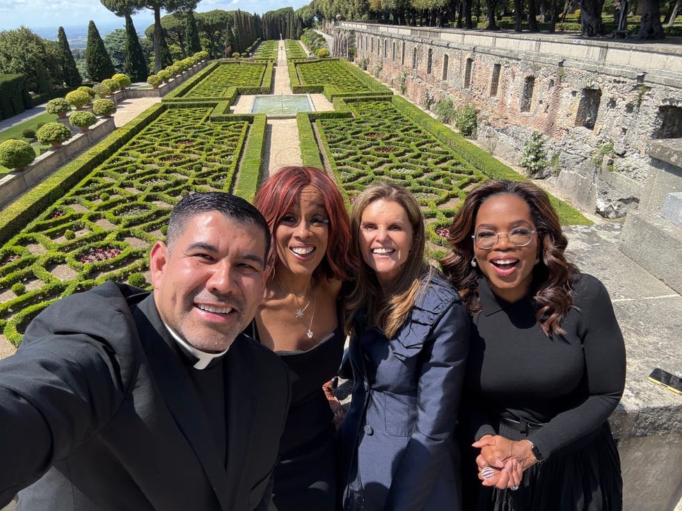 group of people posing for a selfie in a formal setting with manicured gardens in the background