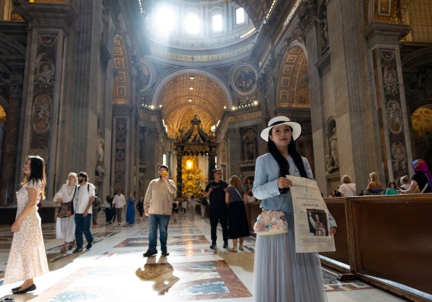 A woman holds a picture of Pope Leo XIV while...