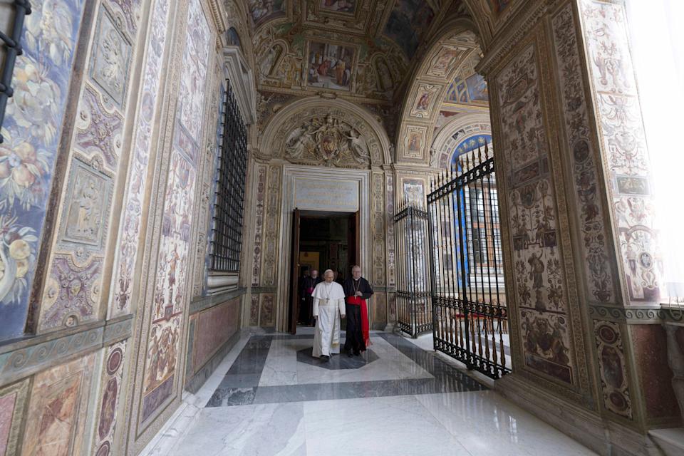 Pope Leo and two others walk through an elaborately decorated corridor