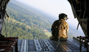 A US soldier sits on the edge of a helicopter looking out.