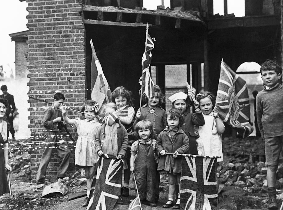 Children waving flags on VE Day, 8 May 1945. 'In bomb scarred Battersea, the little Londoners celebrated V E Day among the ruins of their homes'. (Photo by Daily Herald Archive/National Science & Media Museum/SSPL via Getty Images)