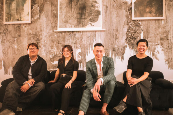 A photograph of four people sitting on a couch in front of a wall of artwork.