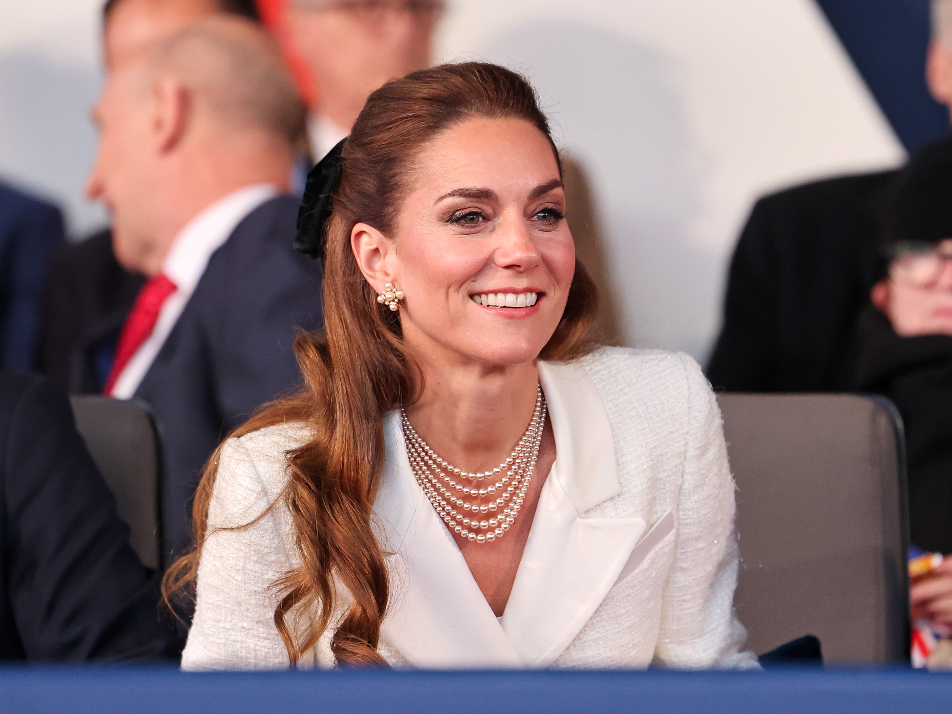Kate Middleton wearing a white blazer with pearls and smiling