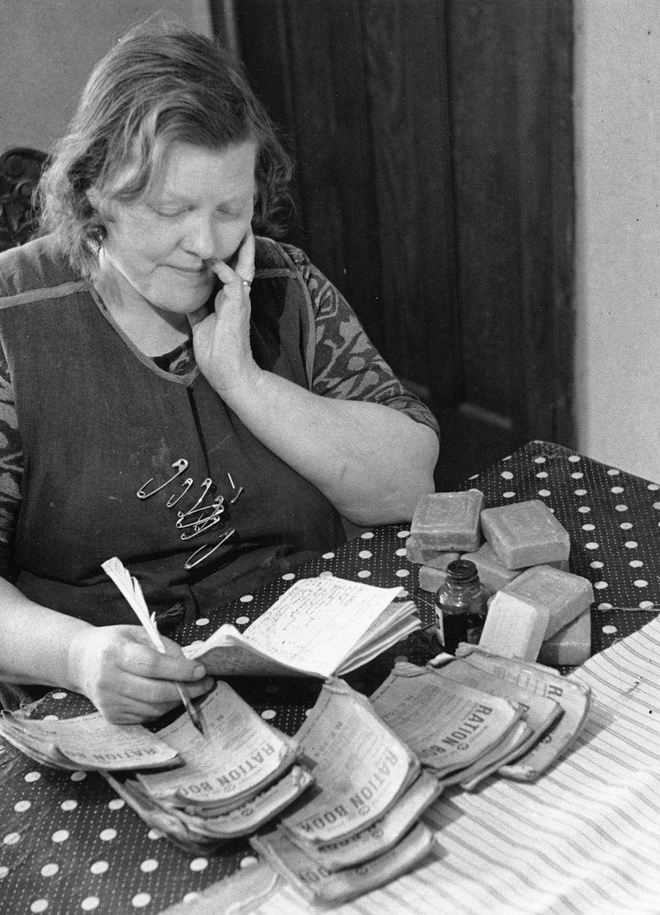 30th June 1945: Safety pins in her apron and with a bottle of ink and a quill pen, Mrs Whitman, mother of sixteen, studies the family's ration books to work out what she can buy. Original Publication: Picture Post - 2017 - Bringing Up A Very Big Family - pub. 1945 (Photo by Kurt Hutton/Picture Post/Hulton Archive/Getty Images)