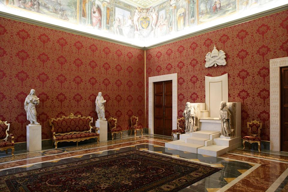 A room with red wallpaper, statues, and ornate furniture