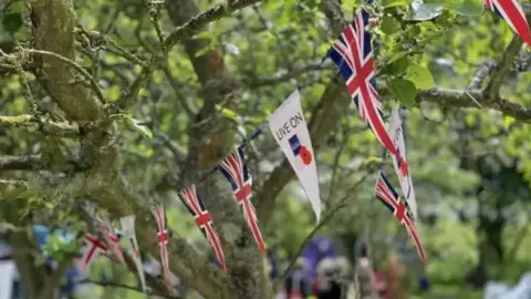 BBC Bunting with the union flag floats in green trees.