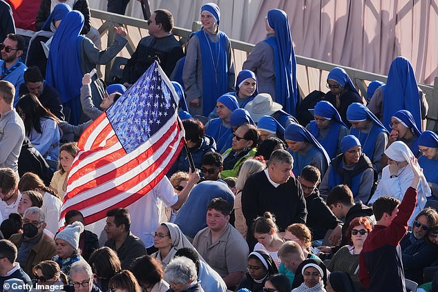 A person holds a US flag as people gather in St. Peter's Square ahead of Pope Leo XIV's inauguration mass