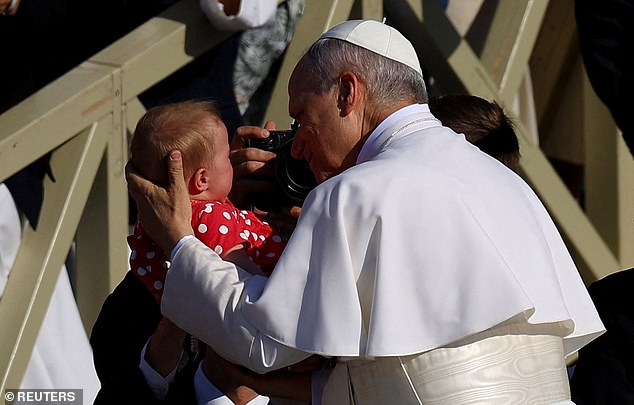 Pope Leo XIV blesses a baby as he arrives on the popemobile for his inaugural Mass
