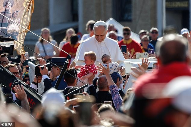 Pope Leo XIV greets the faithful as people hand him babies as he arrives in the popemobile
