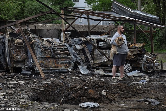 An Odesa resident with a dog stands next to cars destroyed in a residential area during a Russian drone strike