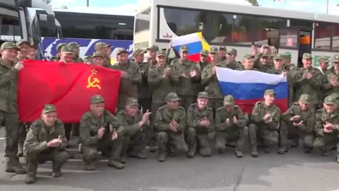 Russian MOD Men wearing Russian uniform gather for a photo holding Russian and Soviet flags