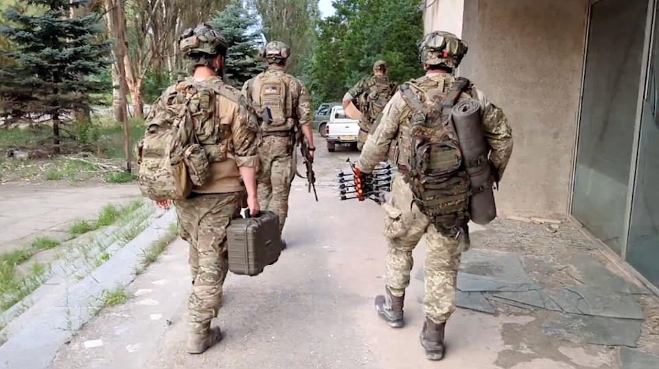Four soldiers in the Ukrainian army seen walking away from the camera holding commercial off-the-shelf drones.