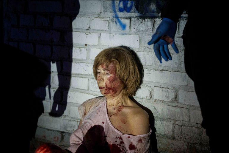 An injured woman sits near her house, which was damaged by a Russian airstrike