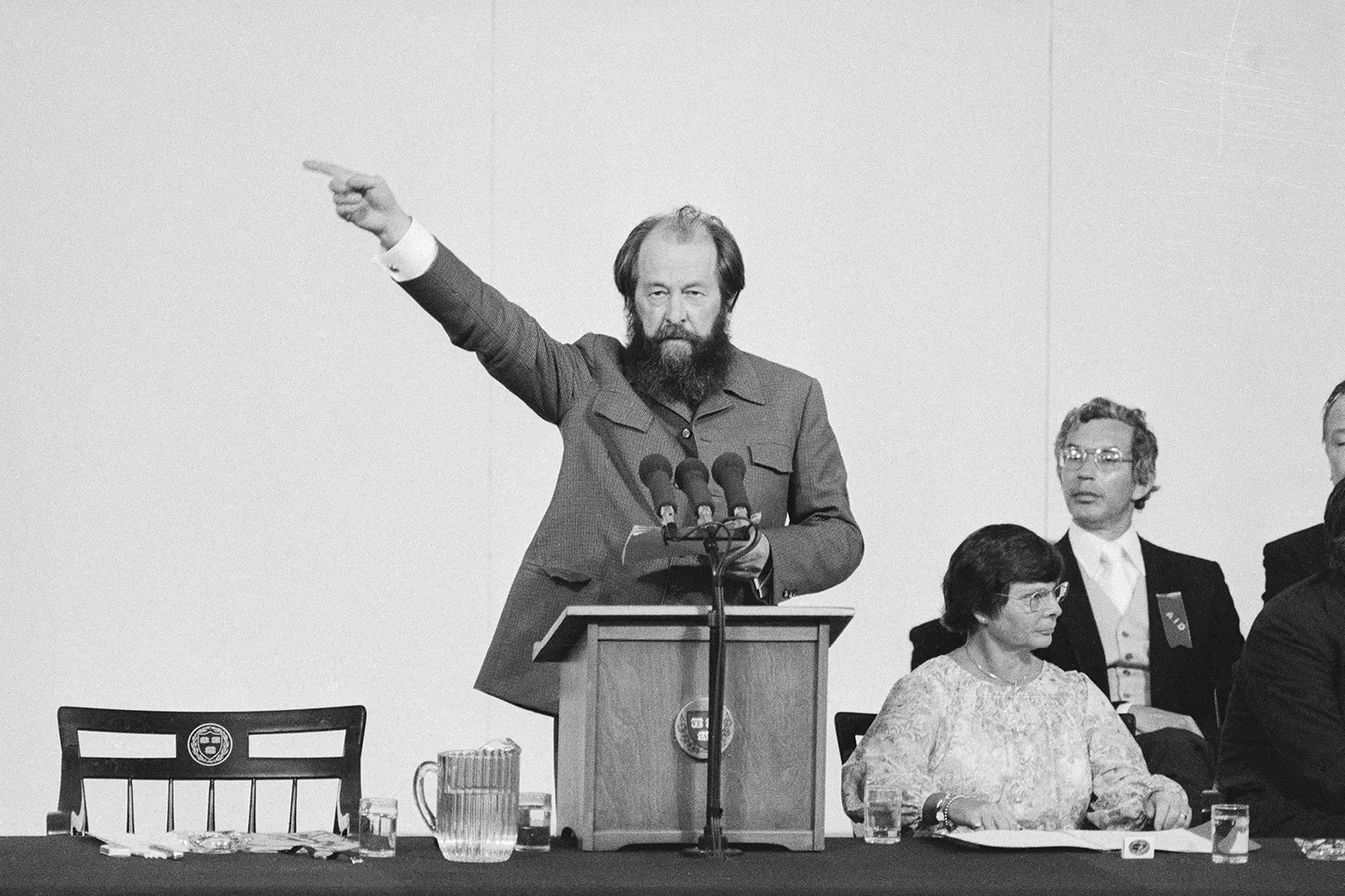 A black and white photo of a man standing at a podium holding his arm out.