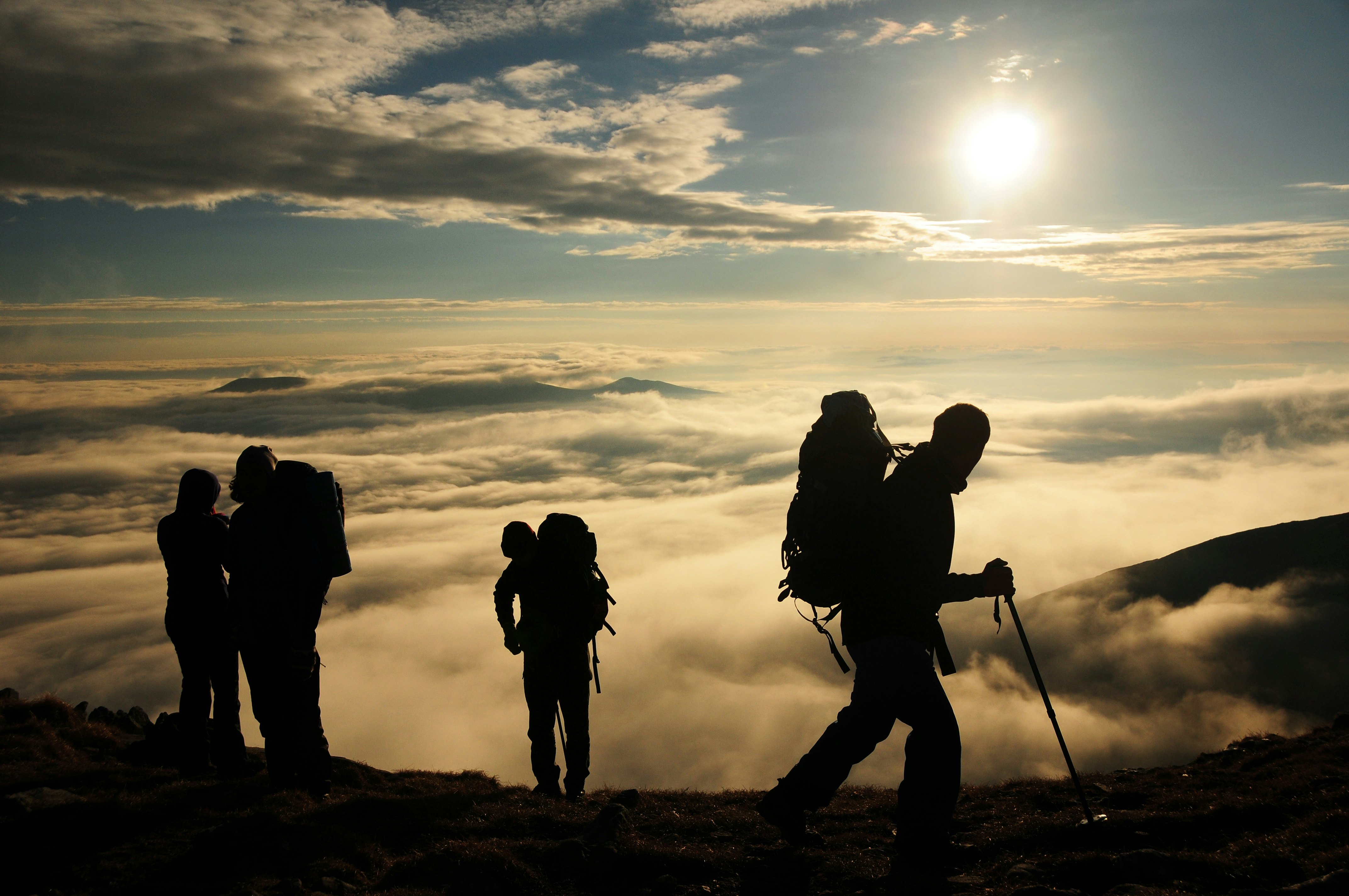 Group of trekkers with backpacks walking on ridge over the clouds at sunset, Malyovitsa peak, Rila National Park, Bulgaria.