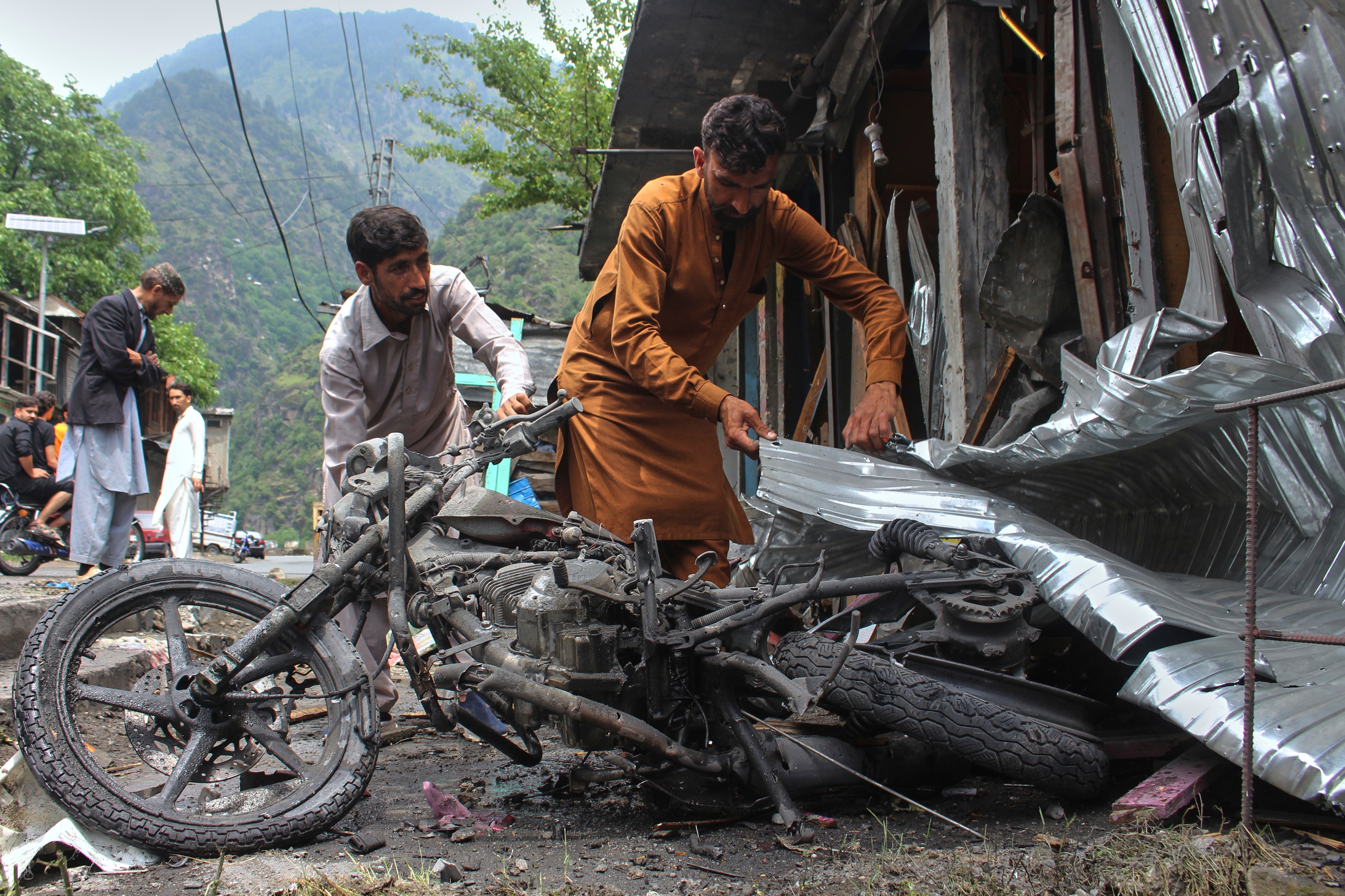 Local residents remove a burnt motorbike from near their shops damaged by Indian shelling, at the main bazaar