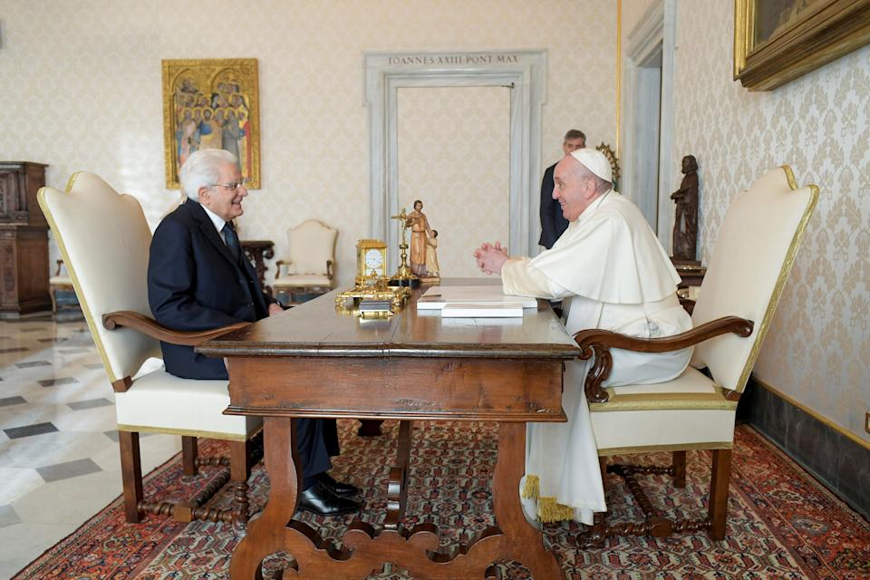Italy's president Sergio Mattarella and Pope Francis sit across from each other at a table in a room with gold and white wallpaper