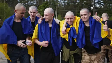 Volodymyr Zelensky/X Five men draped in Ukrainian blue and yellow flags stand together