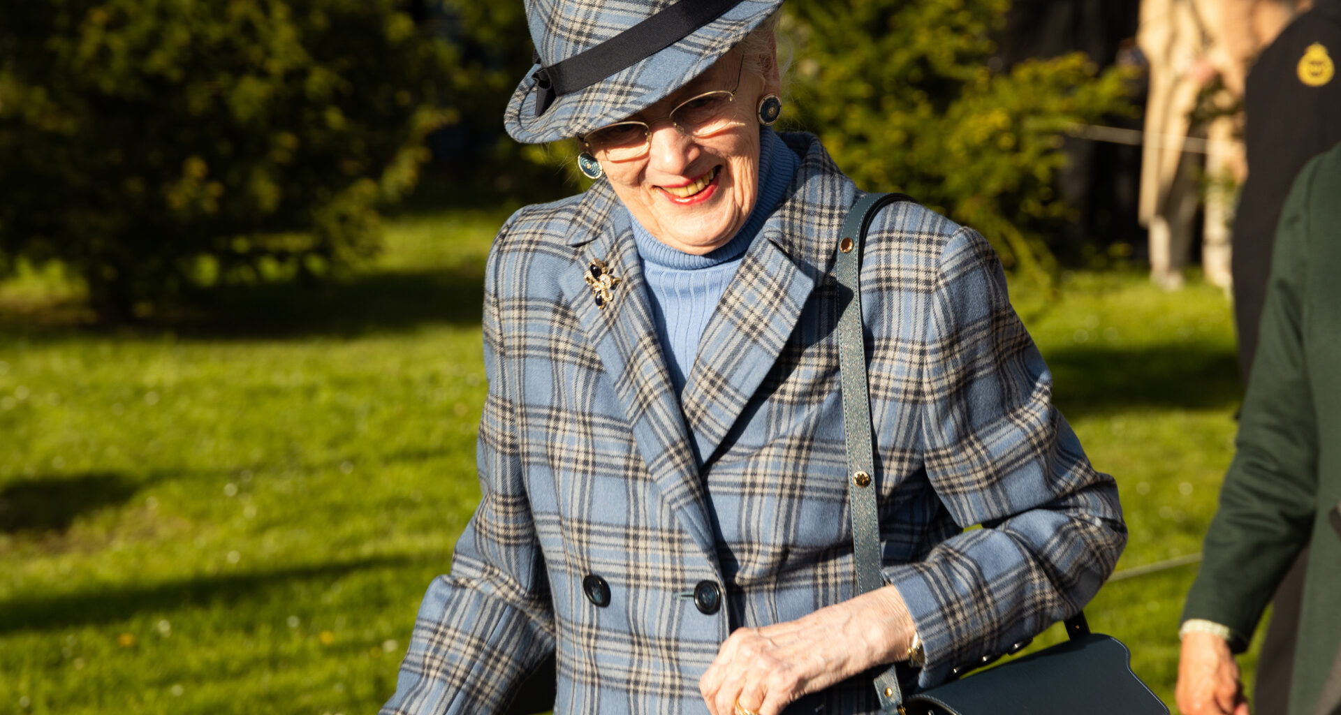 Queen Margrethe wearing a blue plaid coat and matching hat smiling