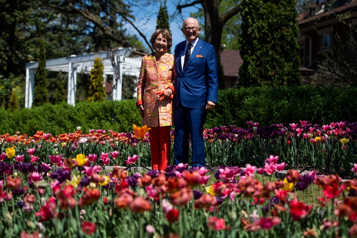 A man and woman stand behind a garden of tulips.