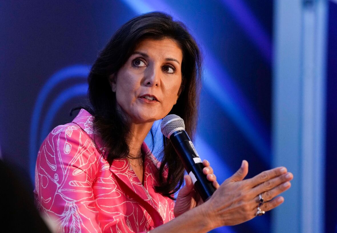 A woman gestures with her hand as she speaks into a microphone.