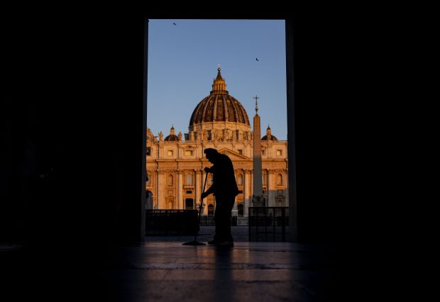A man mops the sidewalk as the sun rises on St. Peter's Basilica on May 16, 2025, days before the installation of Pope Leo XIV at the Vatican. (Brian Cassella/Chicago Tribune)