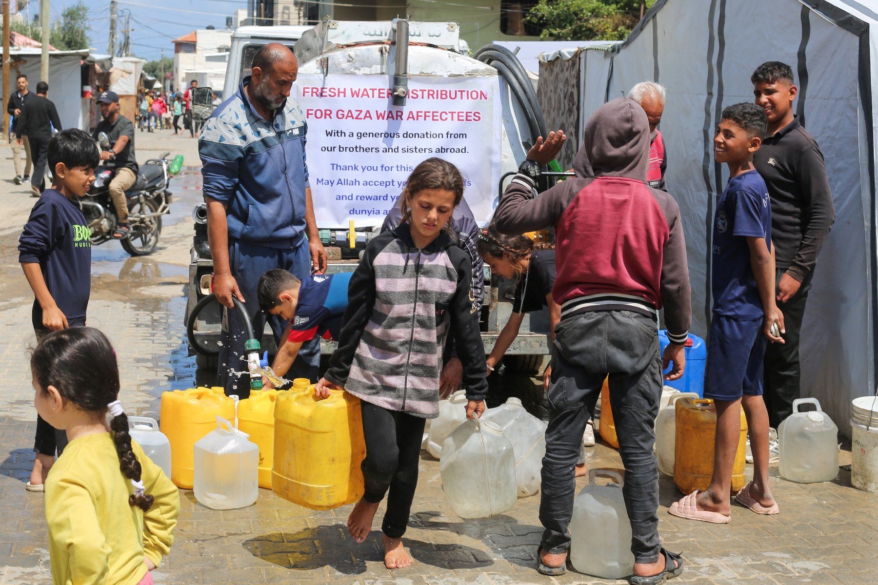 Des enfants palestiniens remplissent des bidons d'eau à un point de distribution au camp de réfugiés de Nousseirat, dans le centre de la bande de Gaza, le 5 mai 2025