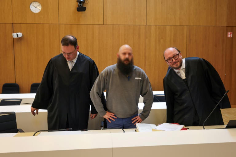 Defendant Dieter S, stands between his lawyers Stephan Schultheis (L) and Michael Loewe (R) as he arrives to his trial for spying for Moscow and readying attacks on critical military infrastructure and industry in a court in Munich, southern Germany, on May 20, 2025. Three German-Russian dual nationals will go on trial in Munich on May 20, accused of spying for Moscow and readying attacks on critical military infrastructure and industry. The main suspect, named only as Dieter S, is said to have been at the centre of a plot to undermine Germany