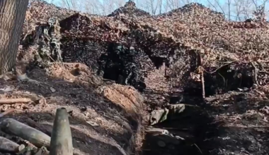 Ukrainian artillery firing from a dugout, while a farmer drives his combine in the field right next to them.