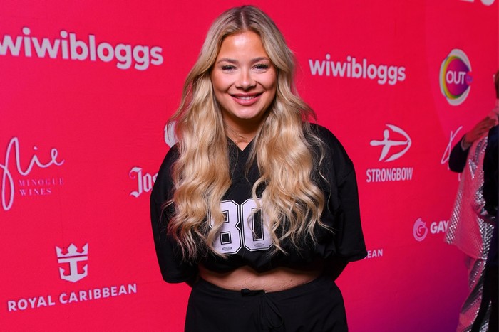 A woman with long curly blonde hair, smiling ahead in a black outfit.