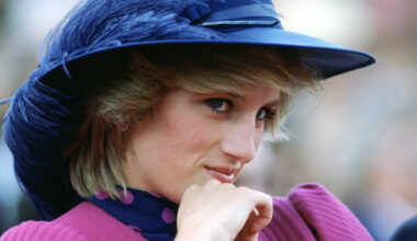 Princess Diana wearing a blue feathered hat and pnik dress leaning her chin on her hand