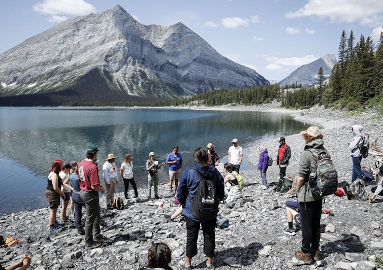Youth standing in front of a body of water listening to a speaker.