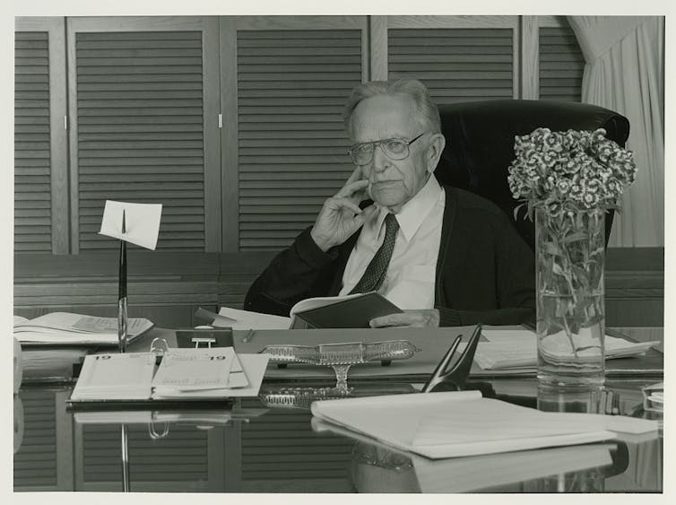 A black and white historical image of an elderly man sitting at his desk