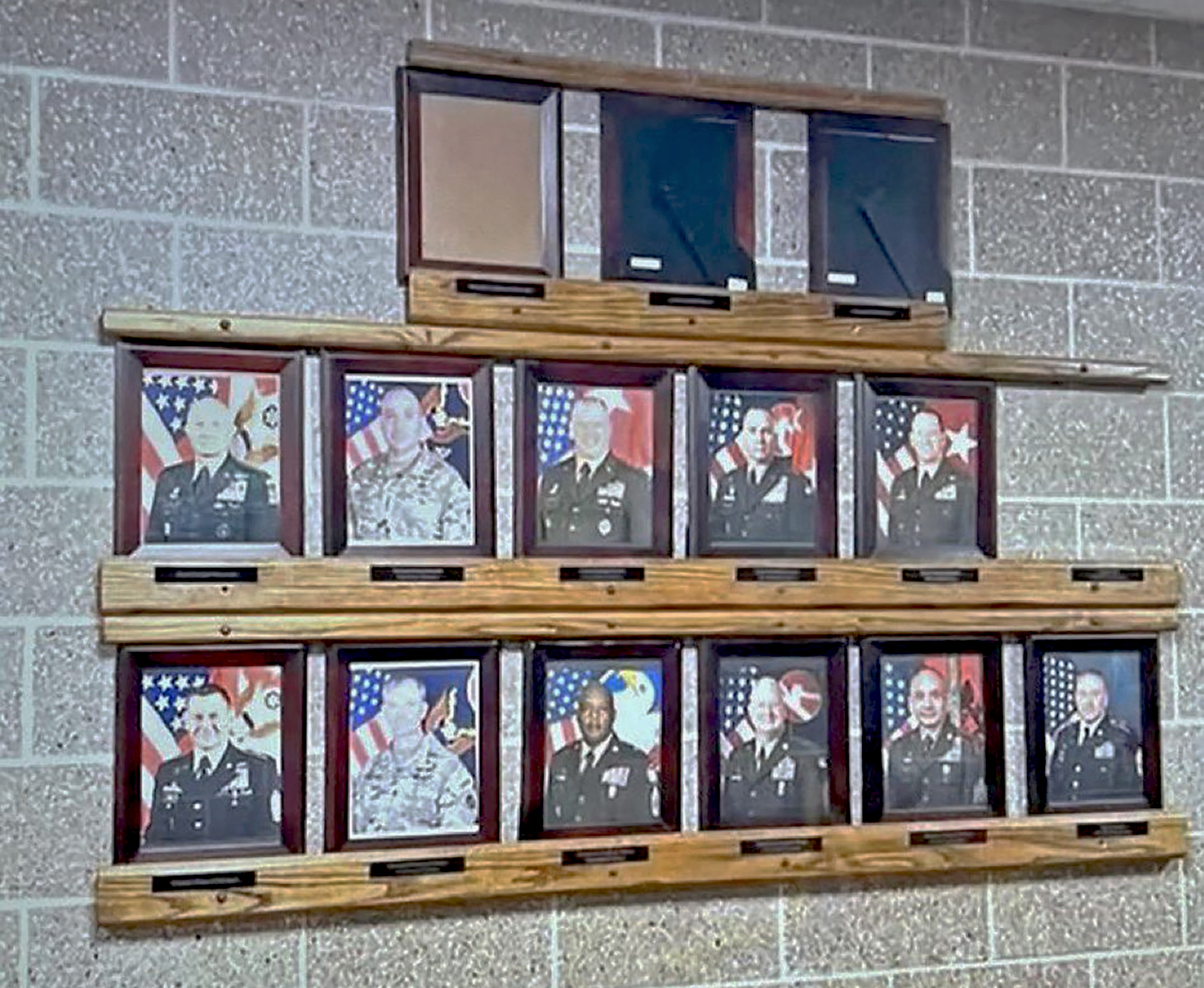 A display of framed military portraits arranged in two rows on a wall, with empty plaques above the top row.