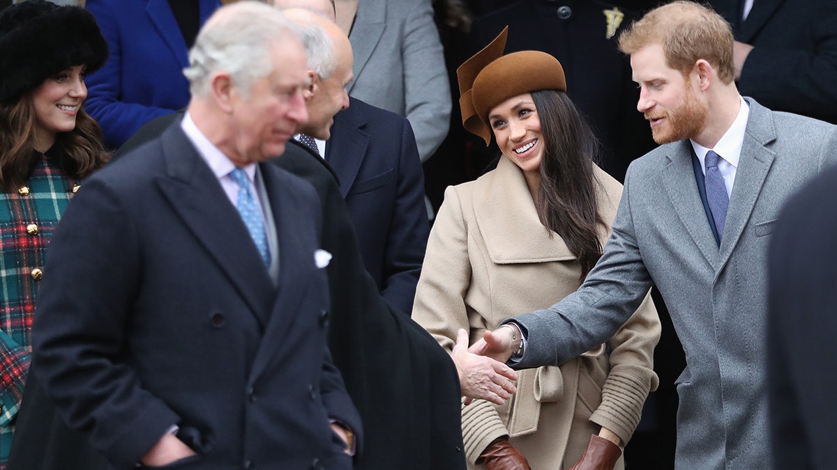 Meghan Markle and Prince Harry shaking hands as King Charles looks on.