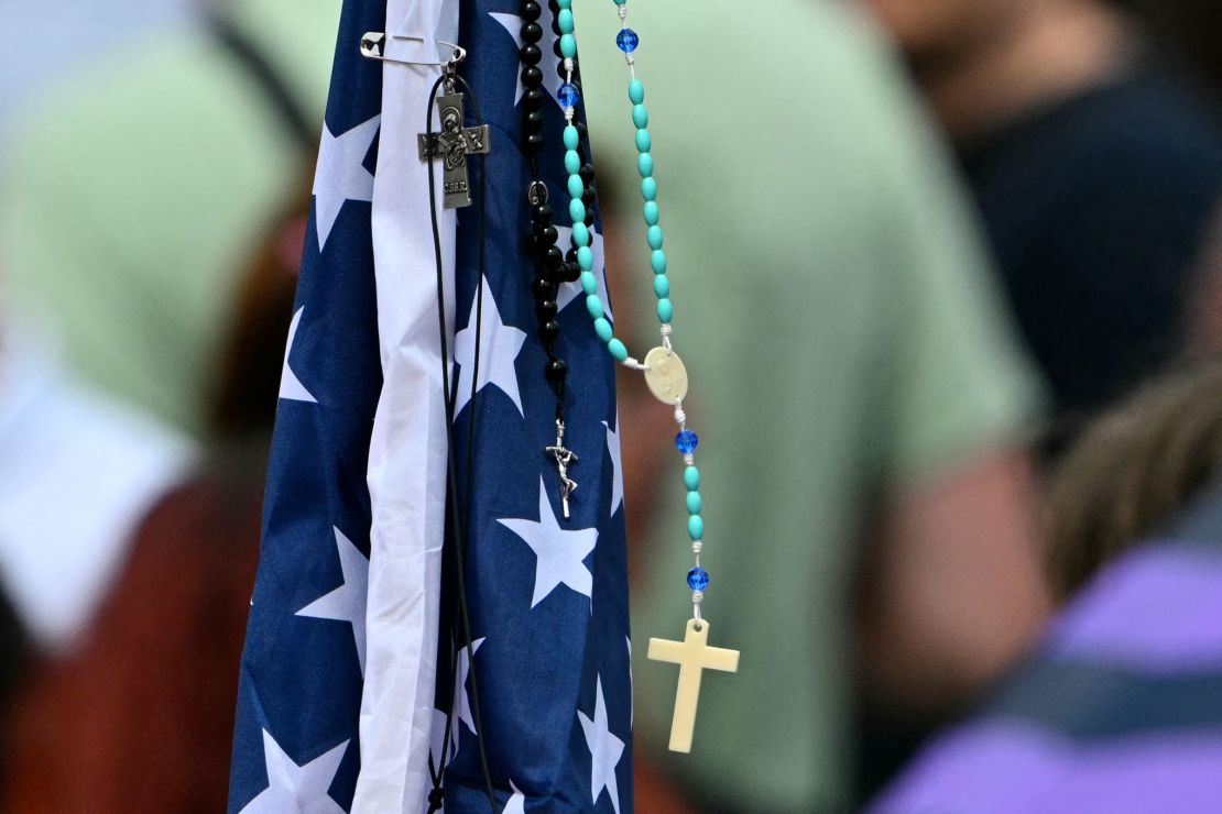 A rosary hangs on an American flag as people gather in St. Peter's Square.
