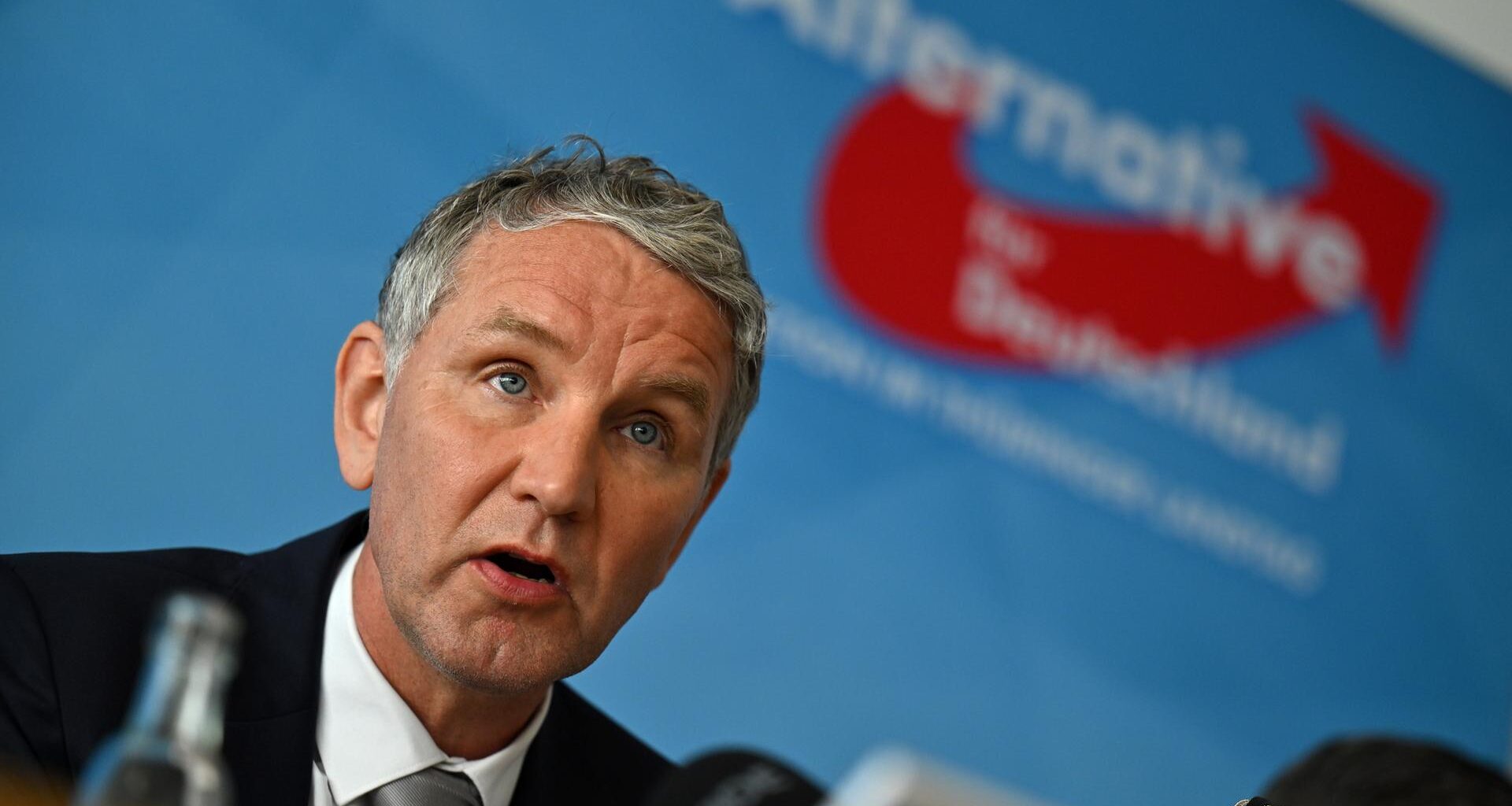 Björn Höcke sitzt vor einer blauen Wand mit dem Logo seiner Partei.