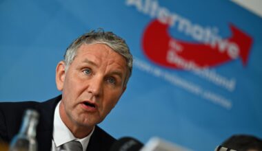 Björn Höcke sitzt vor einer blauen Wand mit dem Logo seiner Partei.
