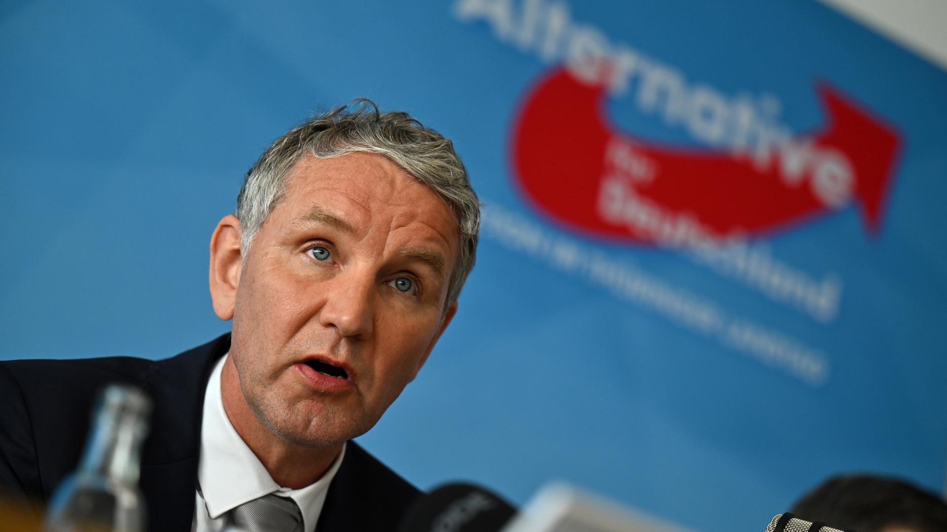 Björn Höcke sitzt vor einer blauen Wand mit dem Logo seiner Partei. Björn Höcke sitzt vor einer blauen Wand mit dem Logo seiner Partei.