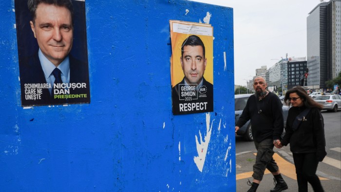 People walk past electoral posters featuring presidential candidates Nicuşor Dan and George Simion